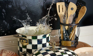 A large pan and a pot on a stove, water splashing out from the large pot, and a set of Mackenzie Childs utensils next to the stove