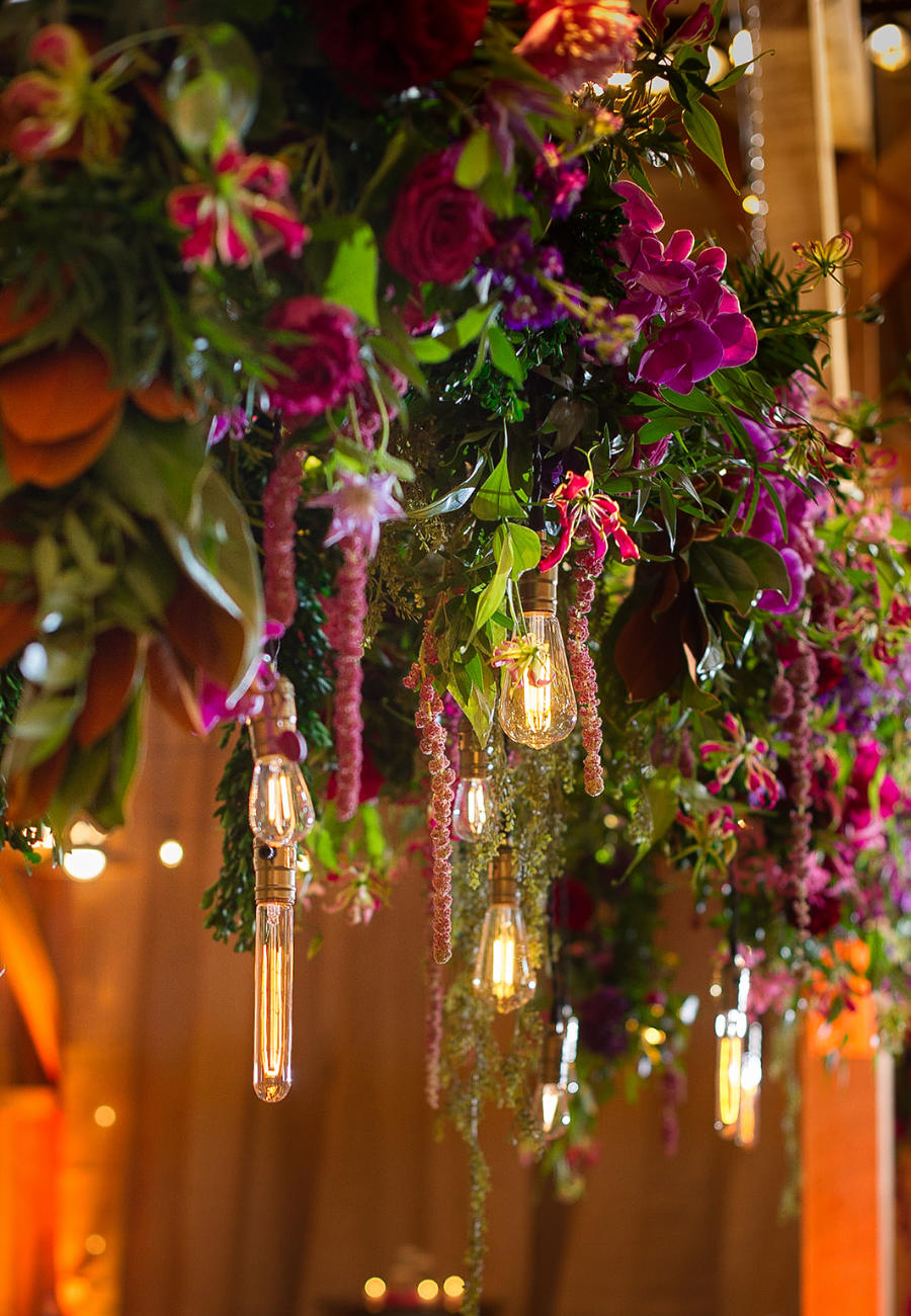 A gorgeous light fixture decoration with deep purple flowers and red roses, and vintage bulb lights for a wedding decoration