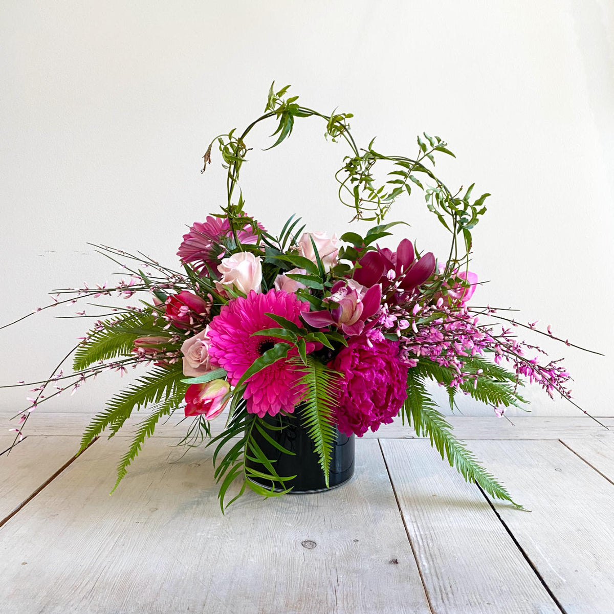 A beautiful flower arrangement in a gloss black vase, featuiring pink roses, orchids and gerbera daisy flowers