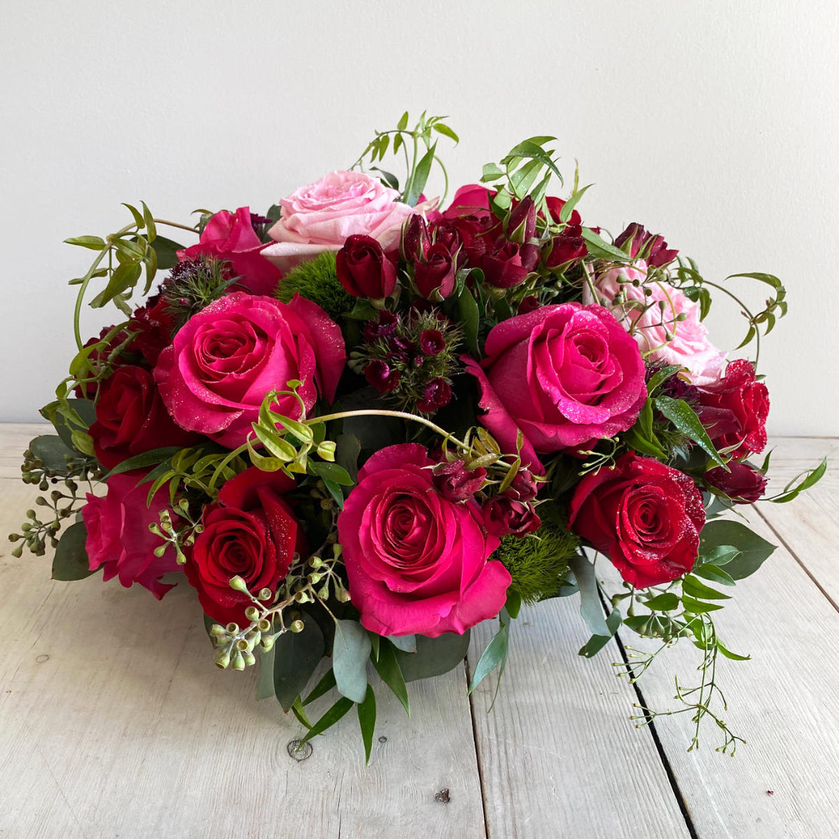 A Jaw-dropping floral design that showcases the pure beauty of a rose. A stunning arrangement of paved mixed roses and greens. Featuring red hearts roses. Pink Floyd Roses and romantic O'Hara garden roses. Topped with a touch of glitter.